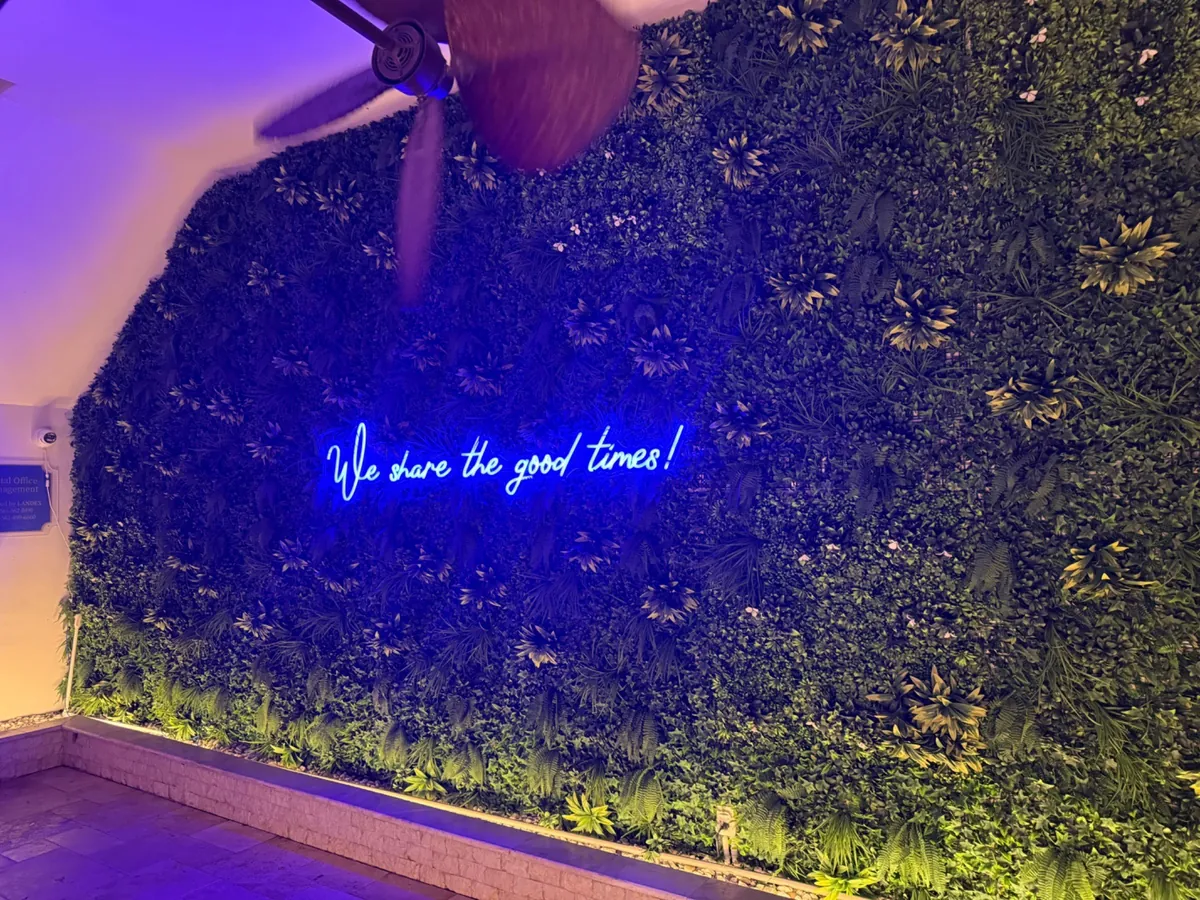 A neon sign reading "We share the good times" glowing on a green wall at night.