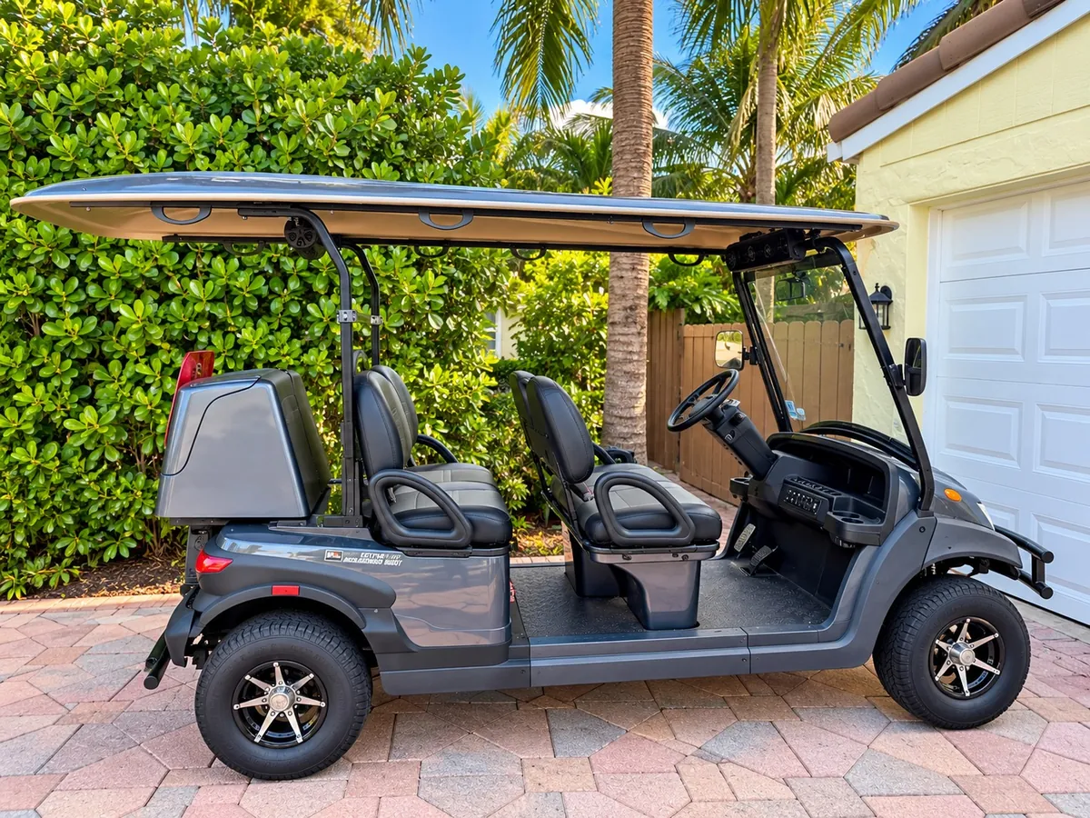 Side profile of a SoFlo six-seat electric cart beside tropical hedging.